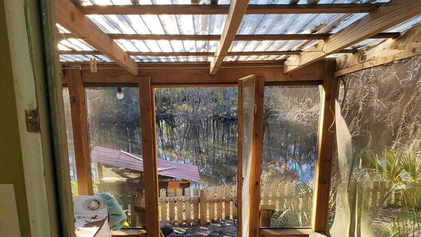 Eine Holzterrasse mit Pergola, die zu einem umzäunten Garten mit Holzzaun und kleiner Gartenhütte führt.