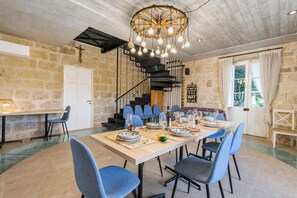 Een eetgedeelte met een lange tafel gedekt voor een maaltijd, omringd door blauwe stoelen, een trap en een stenen muur.
