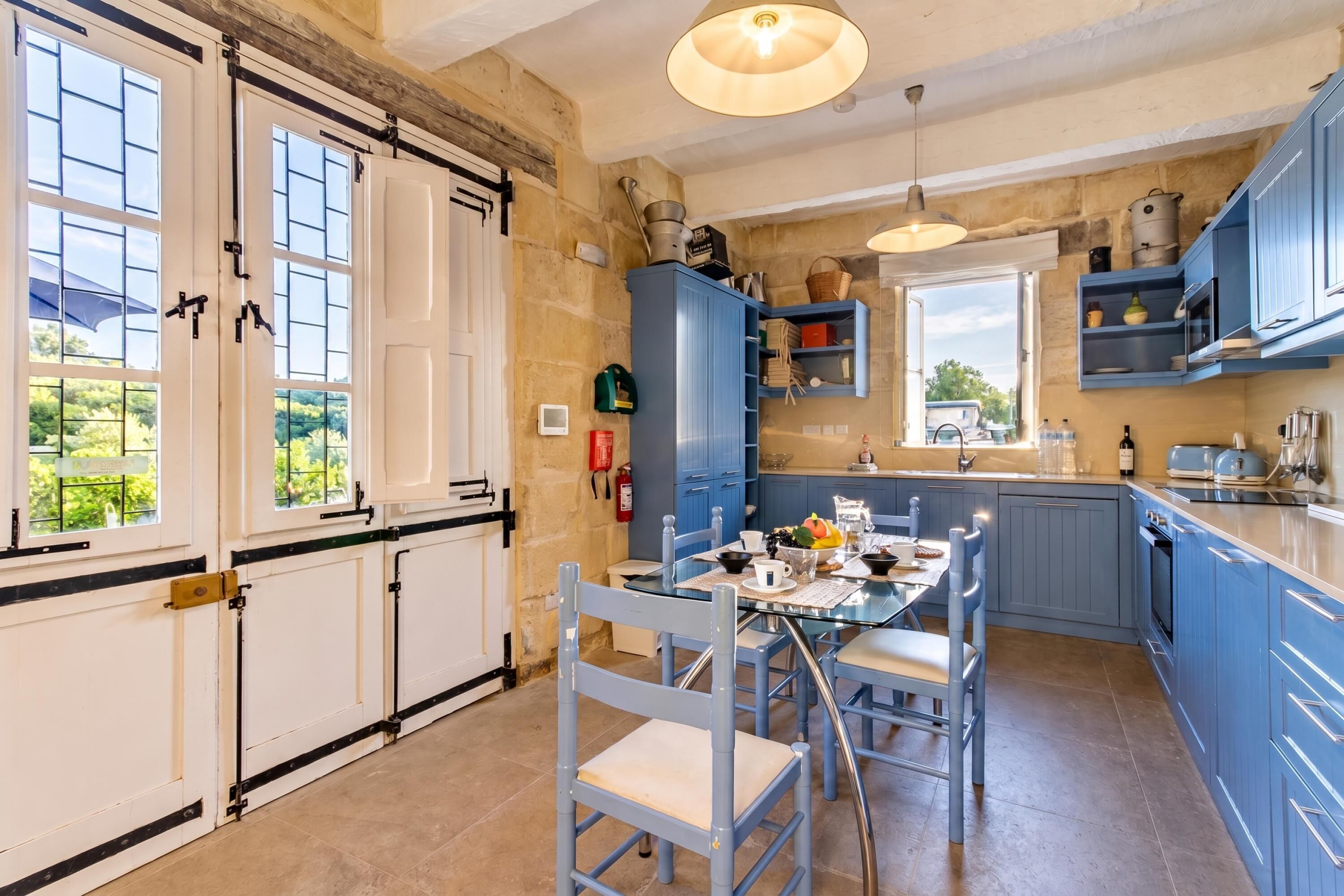 A kitchen with blue cabinets, a dining table with chairs, and a view of the outdoors.