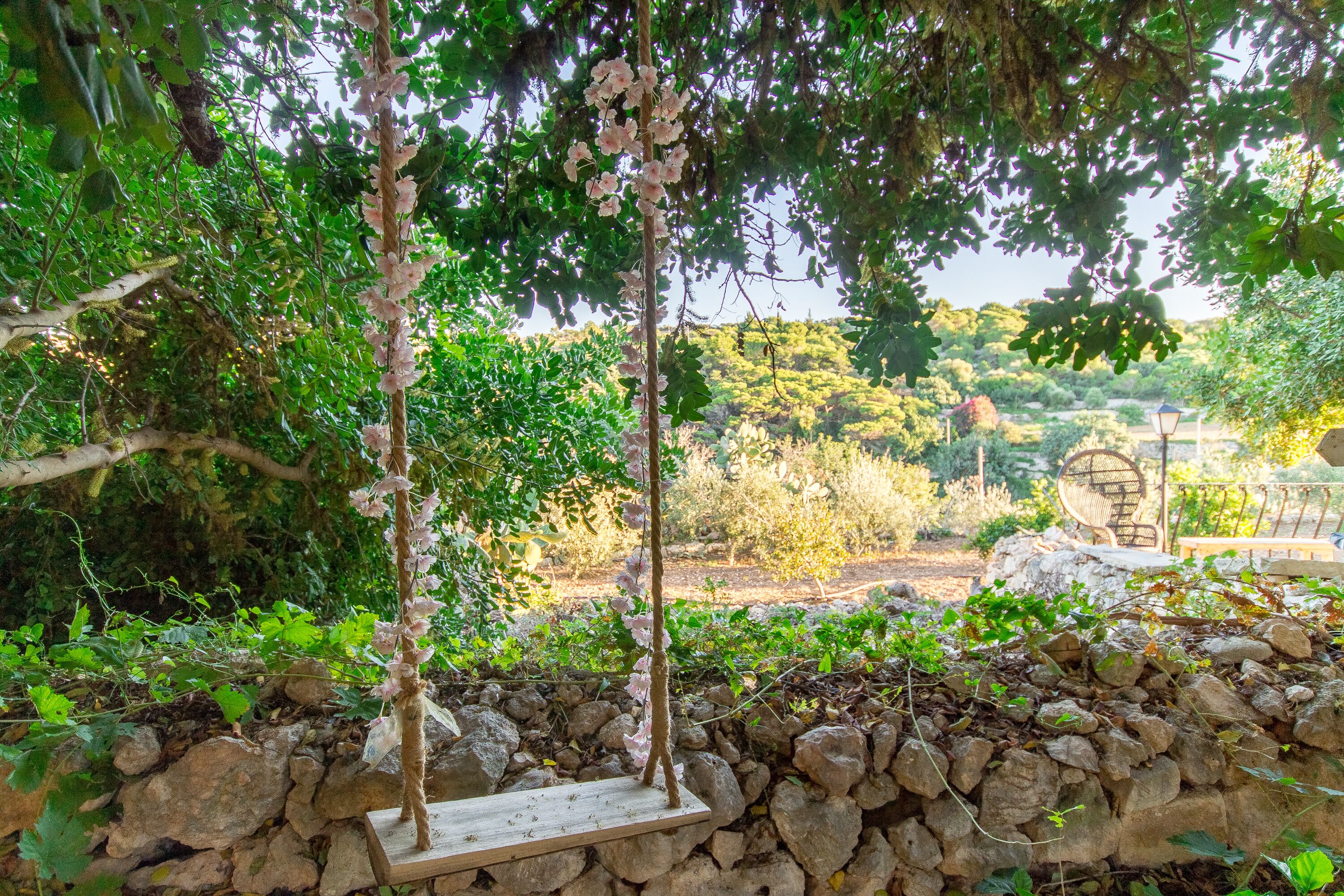 A garden with a stone wall, a wooden swing, and a bench.