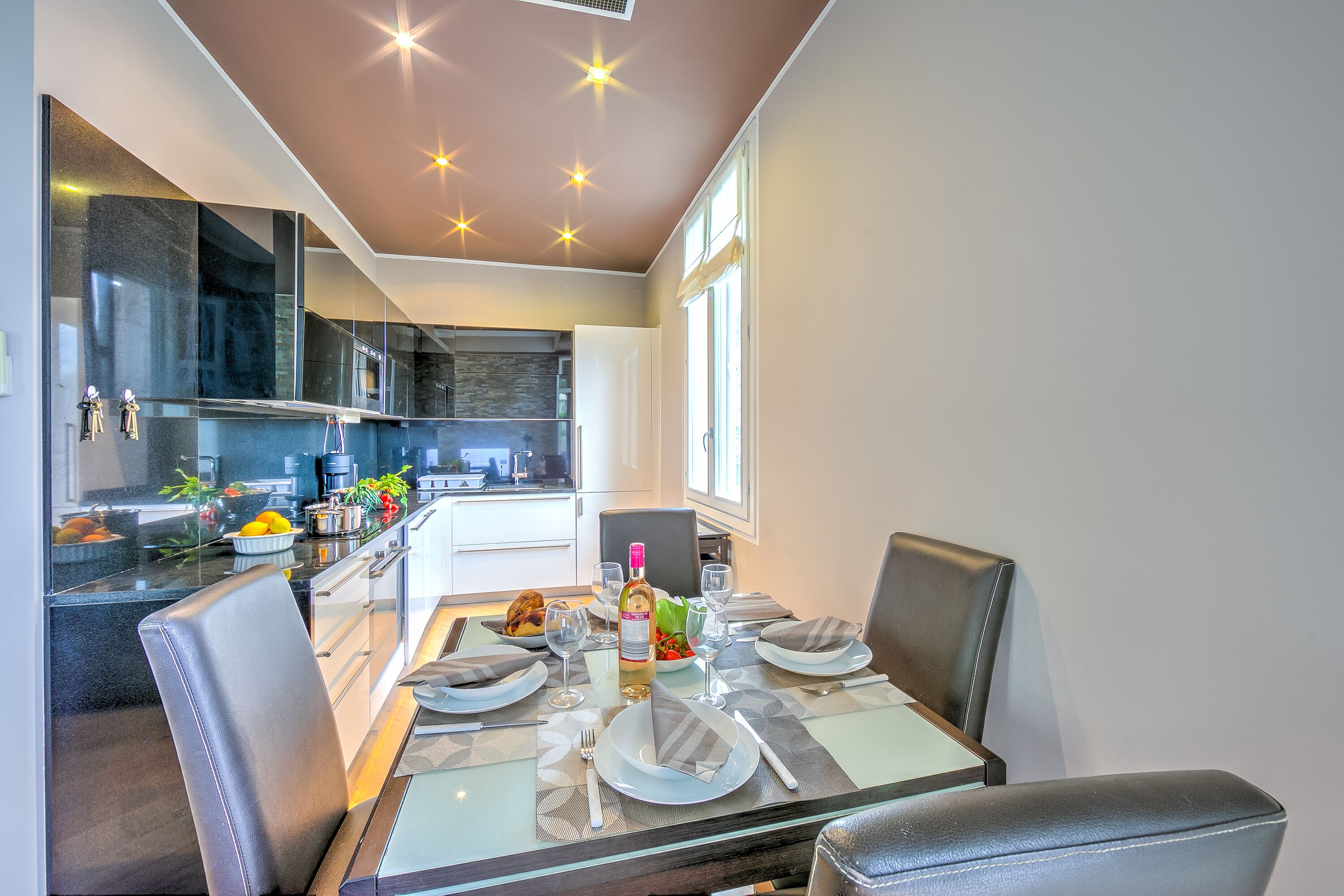 Een moderne eethoek met een glazen tafel, lederen stoelen en een keuken op de achtergrond.