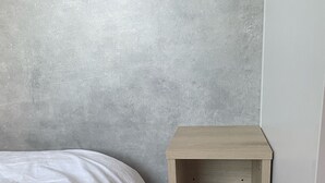 A bedroom with a bed against a textured gray wall and a wooden nightstand with shelves.