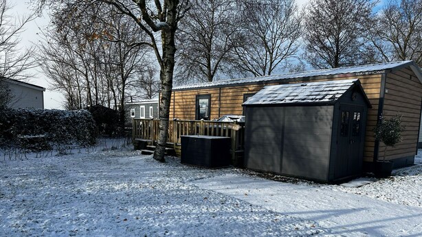 Una cabaña de madera con techo de metal, una pequeña terraza y un cobertizo.