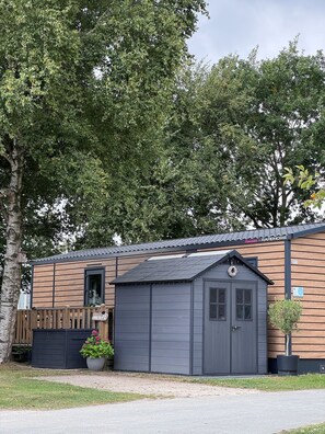 Une petite cabane en bois, dotée d’une porte gris foncé et d’un petit porche agrémenté d’une clôture en bois.