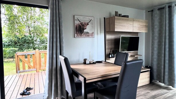 A modern dining area with a wooden table and chairs, a painting of a bull, and a view of a wooden deck and greenery outside.