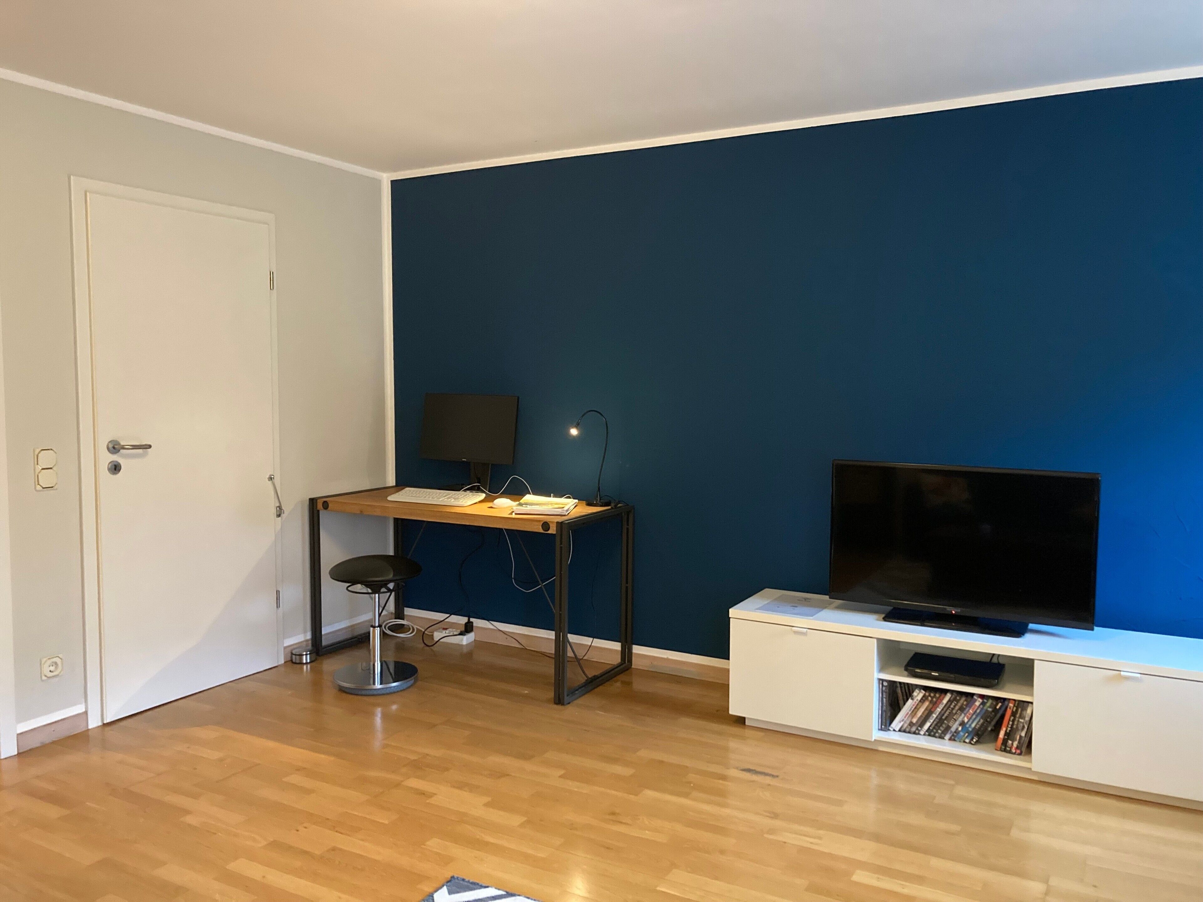 A room with a desk, chair, TV, and a bookshelf.