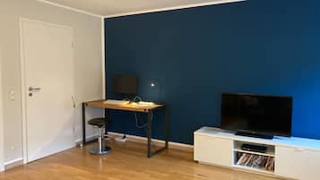 A room with a desk, chair, TV, and a bookshelf.