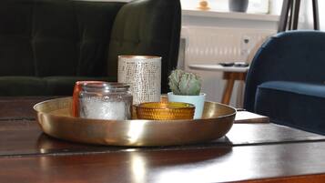 A wooden table with a tray holding a glass jar, a small potted plant, and a woven container. Below the table, there are wine bottles arranged in a rack.