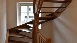 Una escalera espiral de madera con barandilla, que conduce a un rellano con una puerta y una ventana.