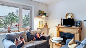 A living room with a sofa, a fireplace, a television, and a window with a view of trees. - Apartment "Haus Excelsior Top 2" with Mountain View, Balcony & Wi-Fi (Seefeld in Tirol)