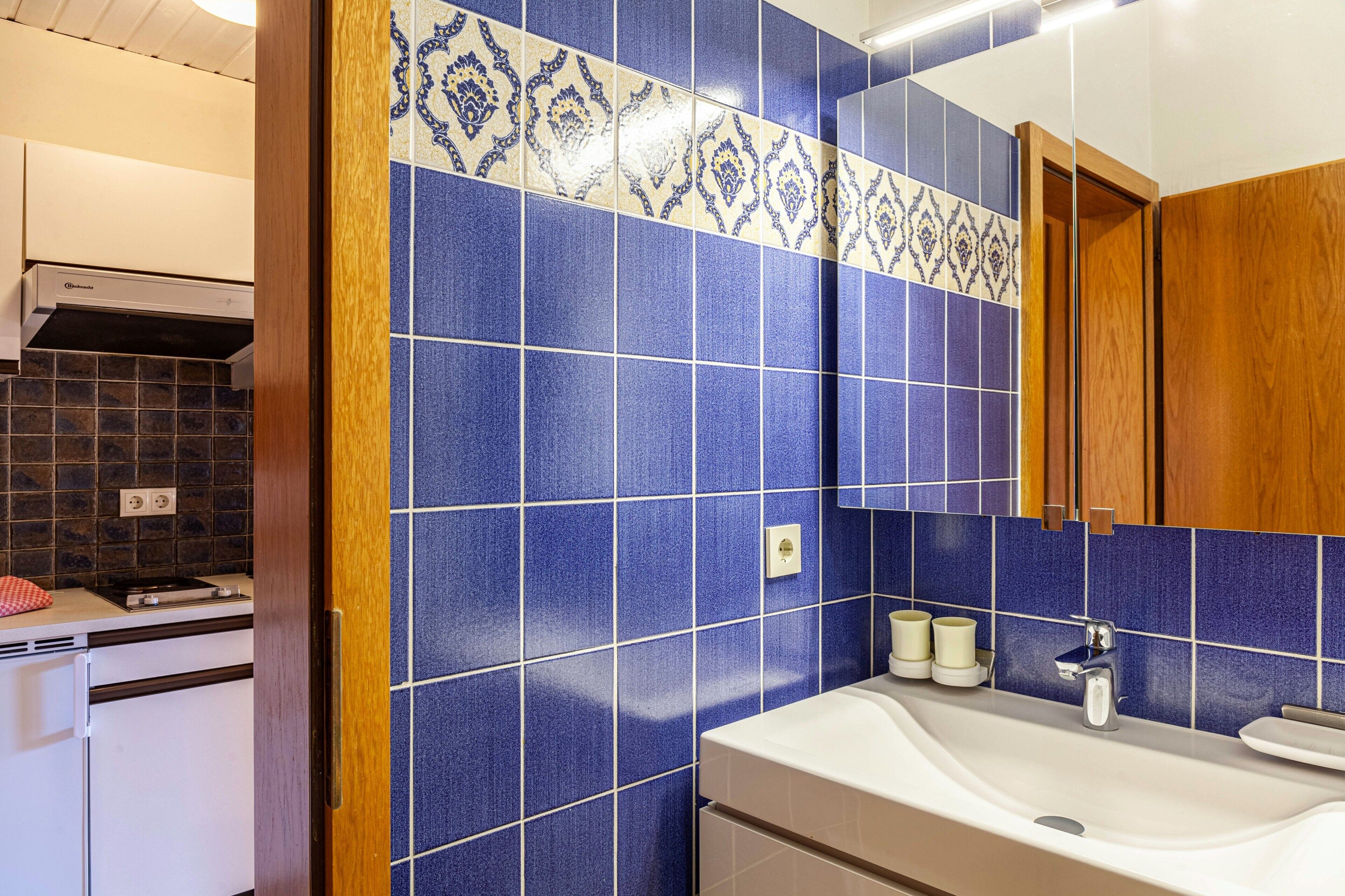 Un baño con azulejos azules, un lavamanos y un espejo.