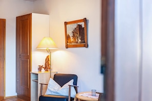 A room with a wooden door, a chair, a table with a glass, and a framed picture on the wall.