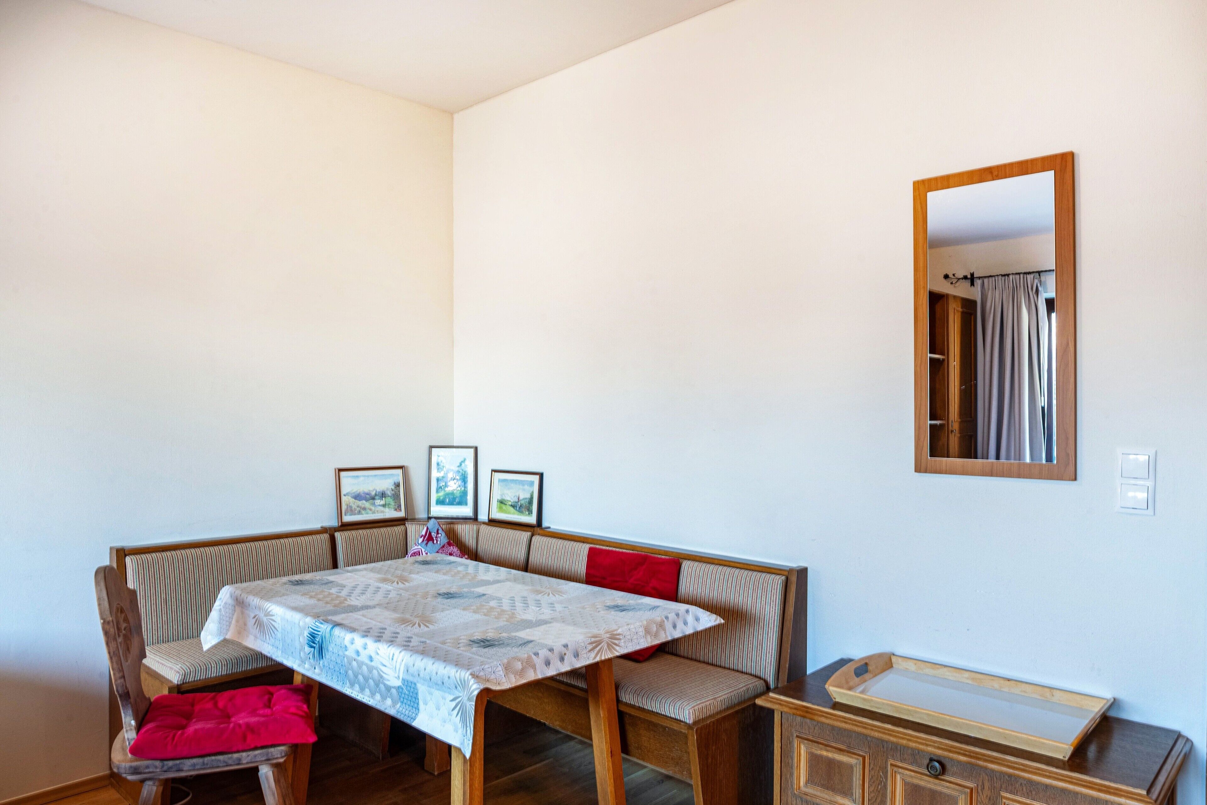 A dining area with a table, bench seating, a mirror, and a small cabinet.