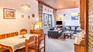 A cozy living room with a wooden dining table, a sofa, a TV, and a window with curtains. - Holiday Apartment "Haus Excelsior Top 5" with Mountain View, Balcony and Wi-Fi (Seefeld in Tirol)