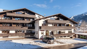 Un hôtel à plusieurs étages doté de balcons, une voiture garée devant et un paysage enneigé en arrière-plan.