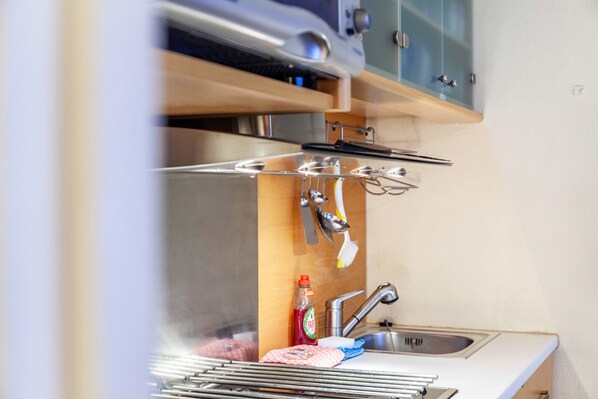 A kitchen with a stainless steel sink, a drying rack, and a bottle of dish soap.
