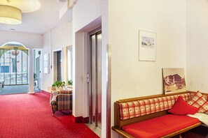 A hotel lobby with a red carpet, a sofa with plaid cushions, and a wall-mounted picture.