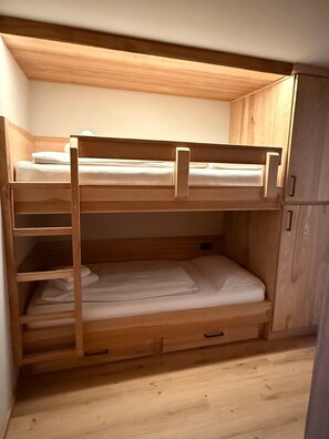 A bunk bed with a wooden frame, a lower shelf, and a wardrobe with a handle.