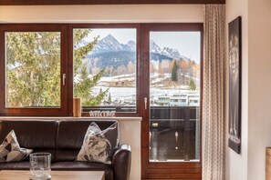 A room with a brown leather sofa, a glass table, and a view of mountains through large windows. - Holiday Apartment "Haus Excelsior Top 21" with Mountain View, Balcony & Wi-Fi (Seefeld in Tirol)