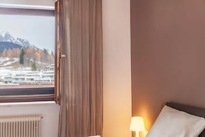 Ein Hotelzimmer mit Fenster, Heizkörper, einem Bett mit Kissen und einer Lampe.