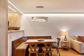 Uma área de refeições com mesa, cadeiras, um banco, um sofá, um abajur e um lustre.