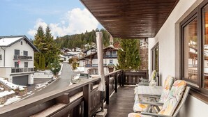 Un balcón con baranda de madera, una mesa con sillas y vista a casas y árboles.