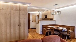 Un espacio habitable compacto con kitchenette, armarios de madera, zona de comedor con mesa y sillas, y un sofá rojo.