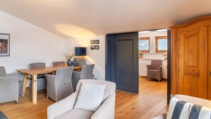 A living room with a sofa, armchair, dining table, and chairs. There is a door leading to a kitchen area. - Holiday Apartment "Haus Excelsior Top 37b" with Mountain View, Balcony & Wi-Fi (Seefeld in Tirol)