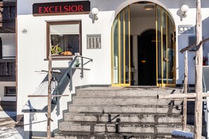 Hotellin sisäänkäynti, jossa on kyltti, jossa lukee ”EXCELSIOR”, portaikko, joka johtaa sisäänkäyntiin, ja ikkuna, jossa on kasvi.