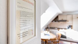 A framed document titled 'Hausordnung' on a wall, with a blurred background of a room with a dining table and chairs. - Apartment "Whg 2 - Vacation on a Country Estate" with Sea View, Shared Garden, and Wi-Fi (Schönhagen)
