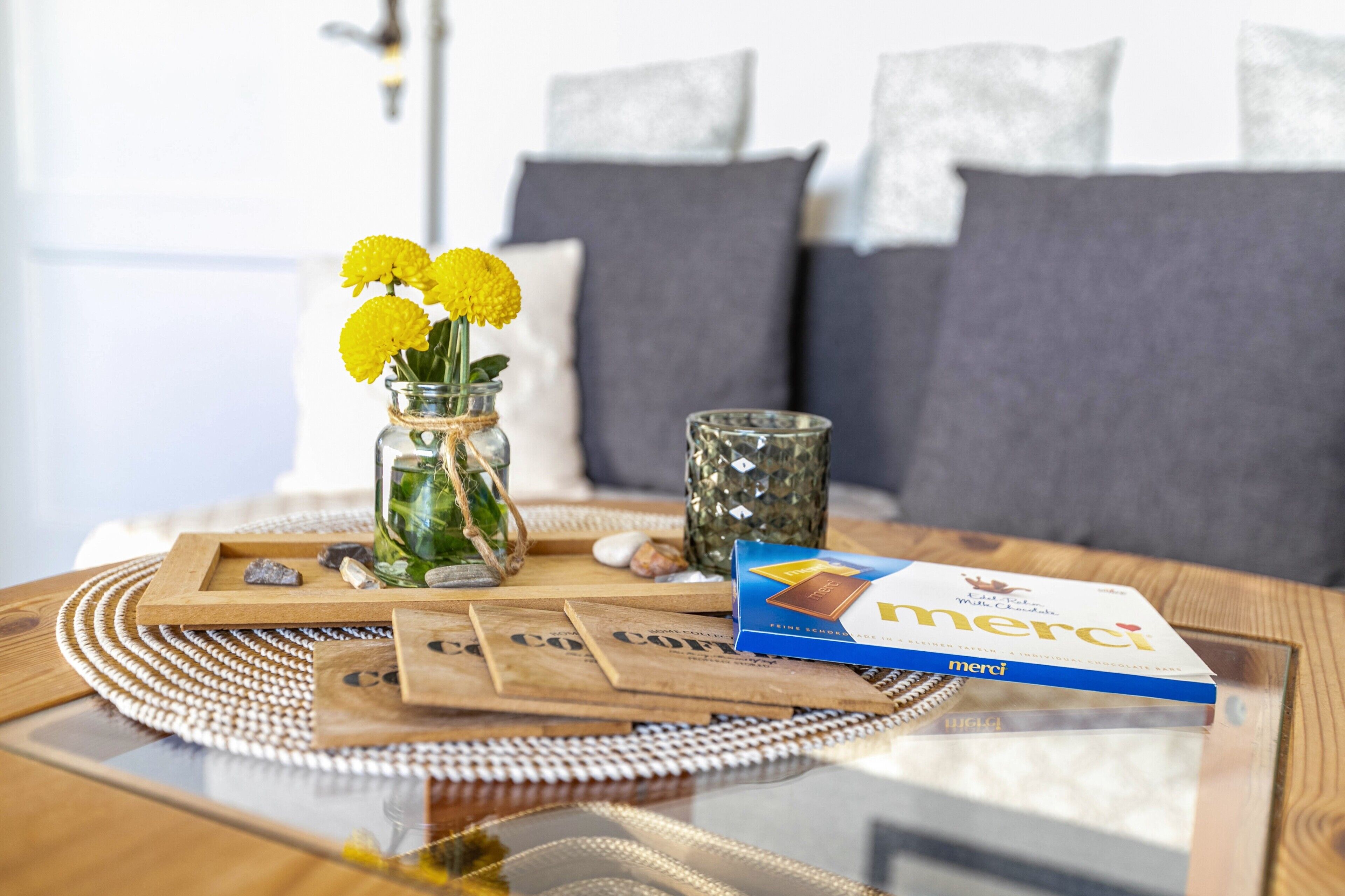 A glass table with a coffee packet, a glass vase with yellow flowers, and a decorative glass container.