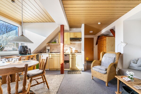 Een gezellige keuken met houten kastjes, een eethoek met tafel en stoelen, en een rieten stoel.