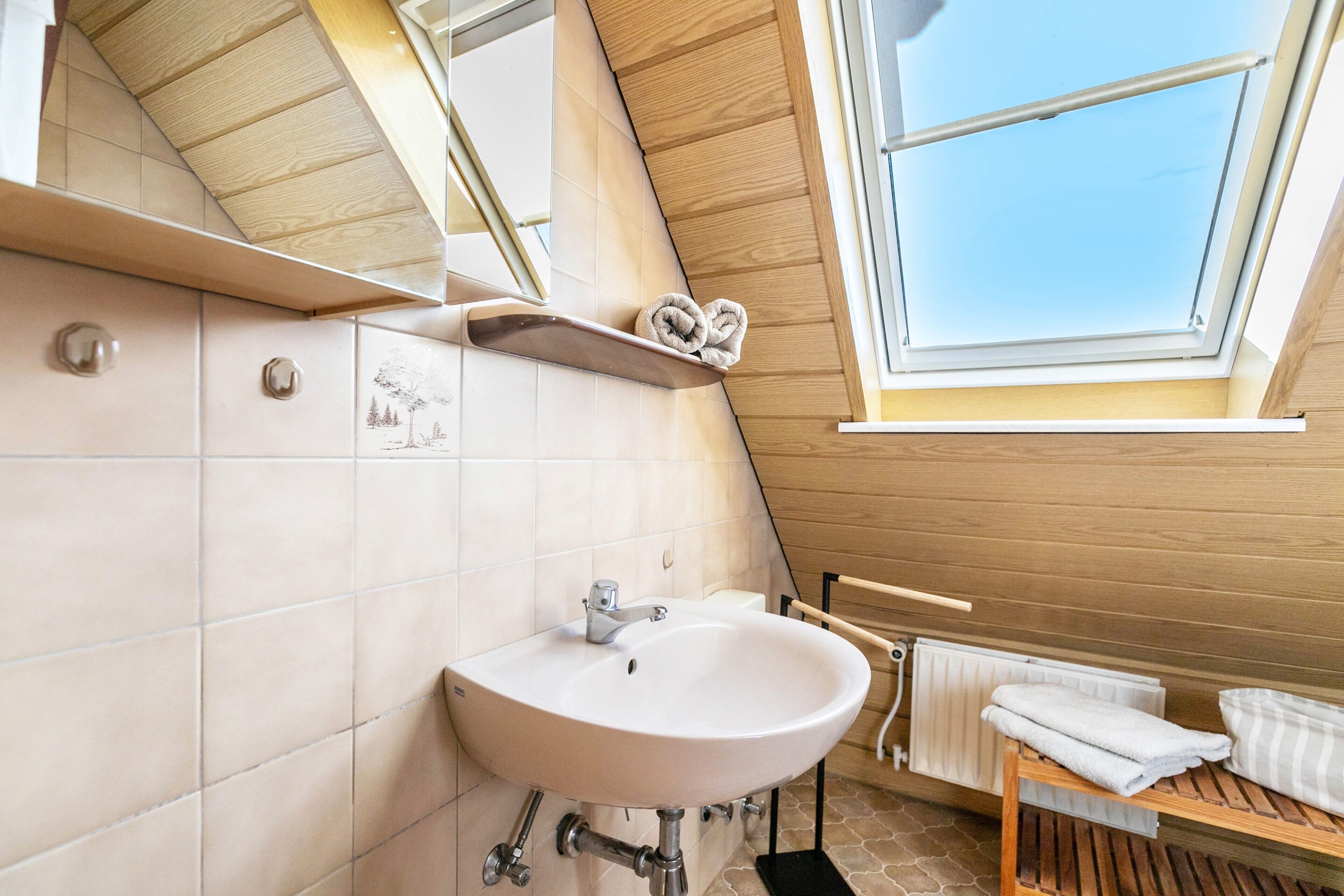 A modern bathroom with a skylight, a white sink, and a wooden shelf with towels.