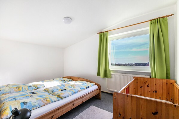 A bedroom with a single bed, a window with curtains, a radiator, and a wooden headboard.