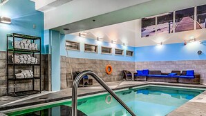 A swimming pool with a glass bottom, a lounge area with blue cushions, and a shelf with folded towels. - Luxury Hotel Room Free Parking, Pool &Hot Tub (Canmore)