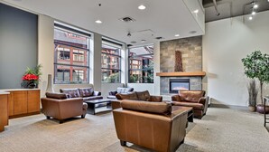 A spacious lounge area with leather sofas, a fireplace, large windows, and a stone accent wall. - Luxury Hotel Room Free Parking, Pool &Hot Tub (Canmore)