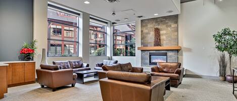 Eine großzügige Lounge mit Ledersofas, Kamin, großen Fenstern und einer Wand aus Stein.
