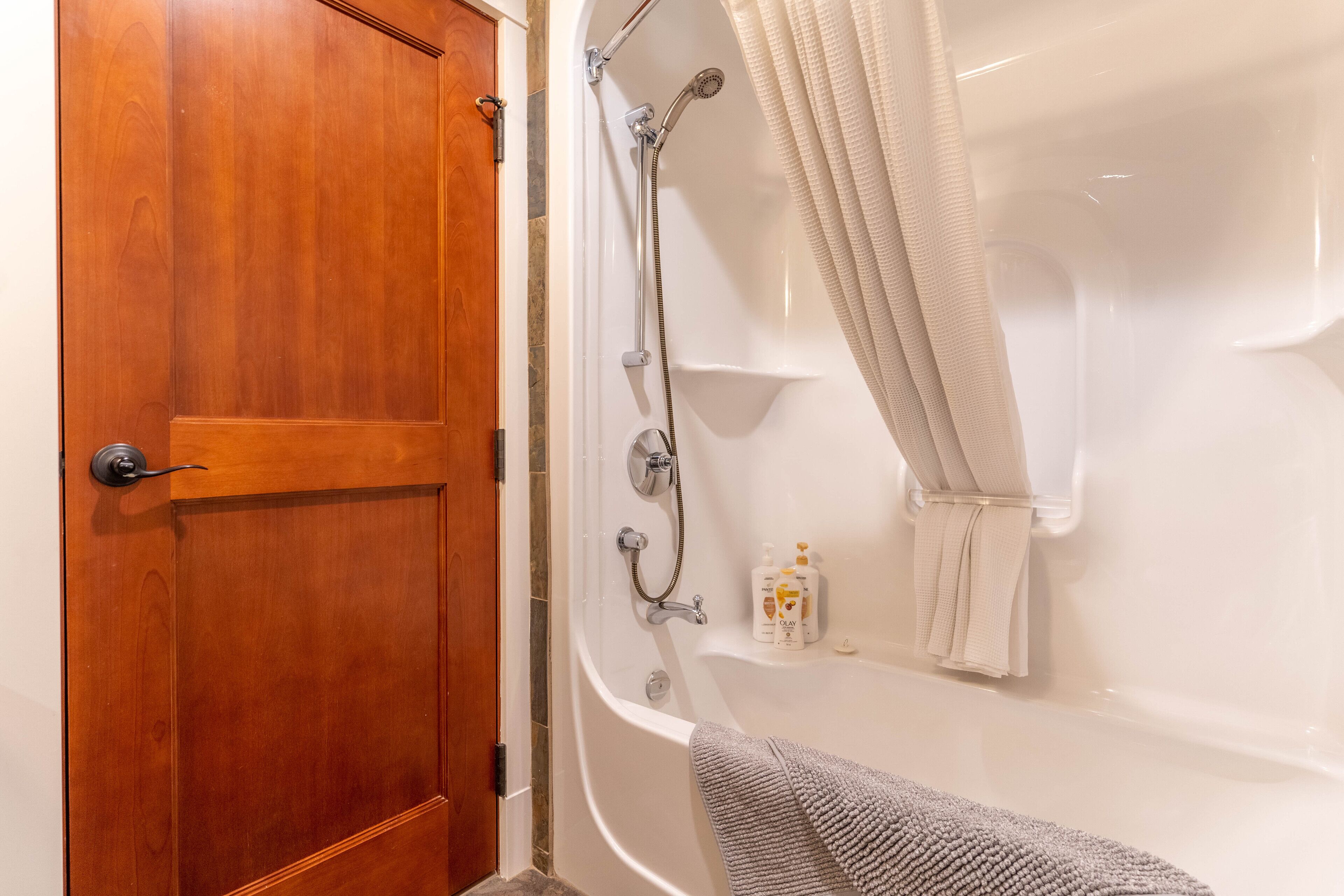 Une salle de bain avec une porte en bois, une baignoire, une pomme de douche et un porte-serviettes.