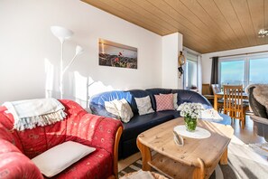 Un salon avec un canapé rouge, un canapé bleu, une table basse en bois et un tableau accroché au mur.