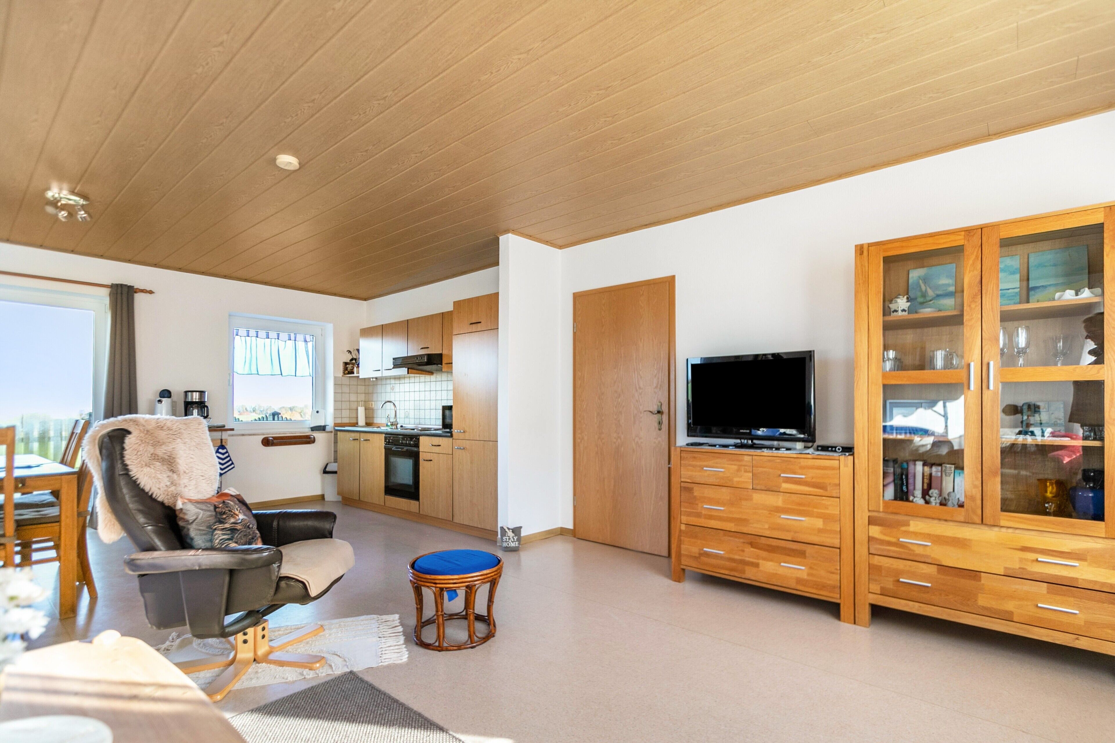 A modern living room with a flat-screen TV, a leather chair, a dining area, and a kitchen in the background.