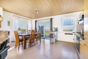 Une cuisine moderne avec des meubles en bois, un coin repas comprenant une table et des chaises, et une vue à travers la porte vitrée.