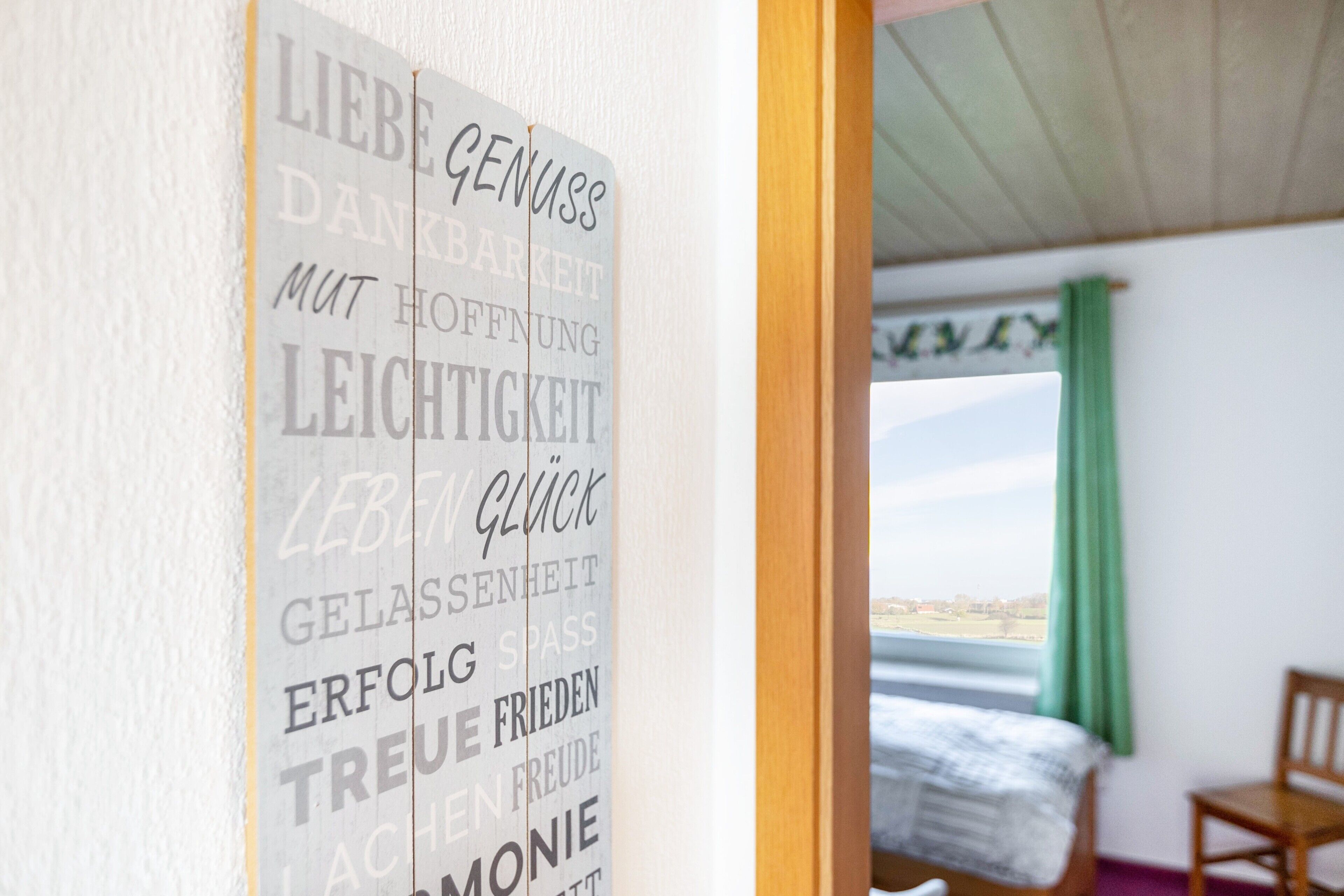 Een kamer met een bed, een stoel en een muur met motiverende woorden in het Duits.