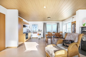 Et moderne køkken med træskabe, et spiseområde med et bord og stole, og en fletstol med hynde.