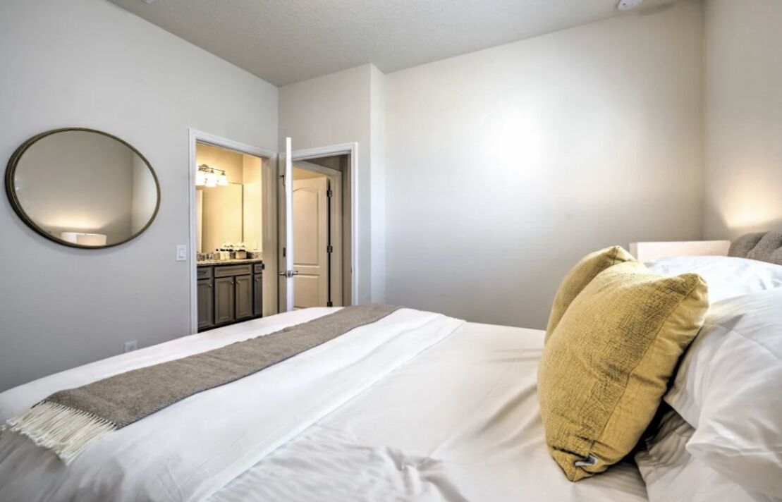 A bedroom with a bed, a round mirror, and a door leading to a bathroom.