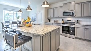 Eine moderne Küche mit Granit Arbeitsplatten, Edelstahlgeräten und einer zentralen Kochinsel mit Barhocker.