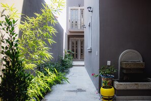 Un callejón estrecho con la entrada de un edificio, plantas en macetas y un barril amarillo.