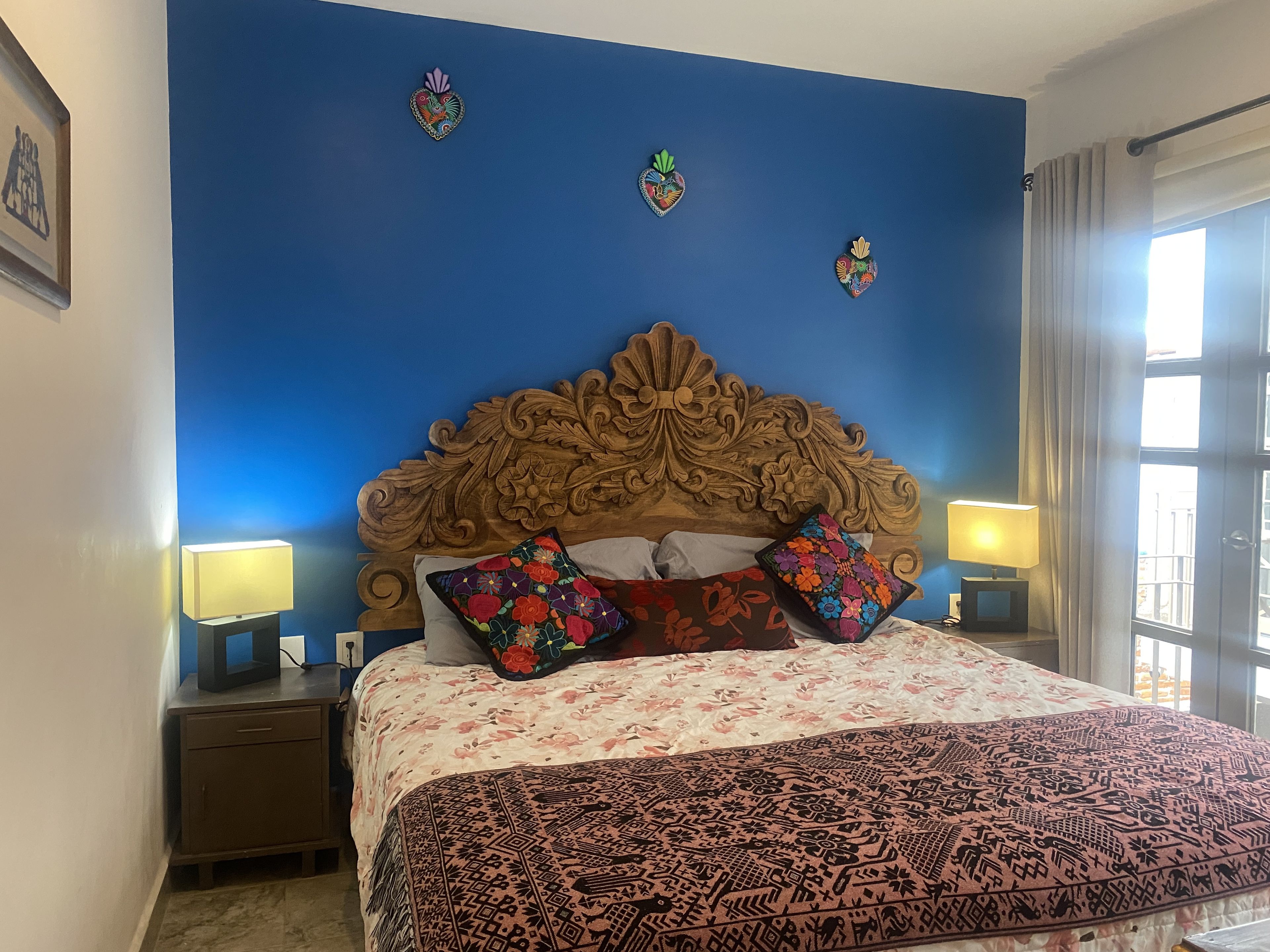 A bedroom with a large bed, two bedside lamps, and a window with curtains.