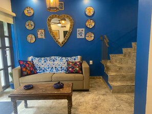 Un salon avec un mur bleu, un canapé, deux coussins, une table basse, un miroir en forme de cœur et un escalier.