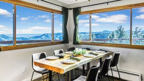 Ein Essbereich mit einem Holztisch, gedeckt für sechs Personen, großen Fenstern mit Blick auf die Berge und einer darüber hängenden Chandelier.