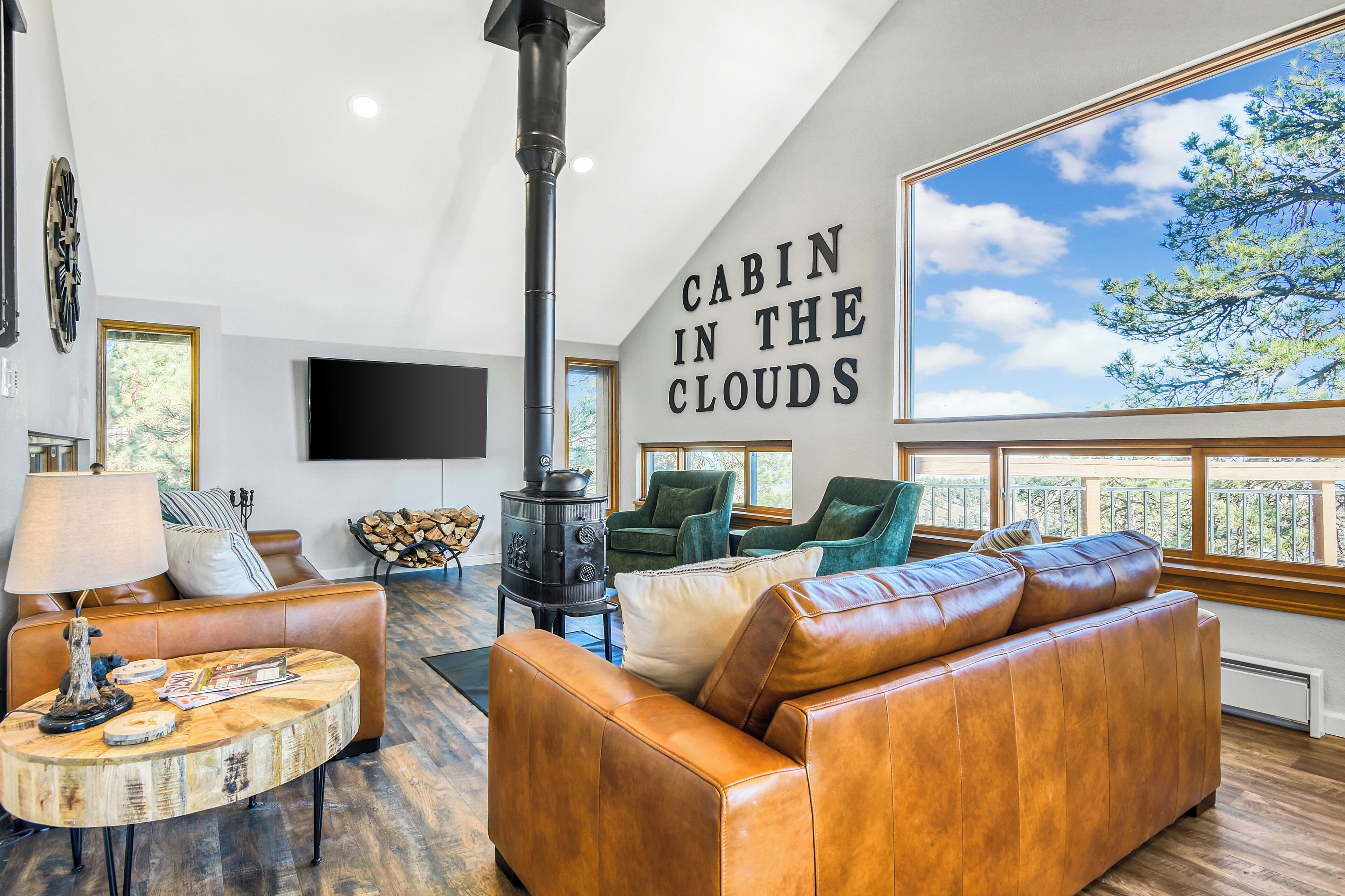 A modern living room with a large window, a fireplace, leather furniture, and a wall-mounted TV.